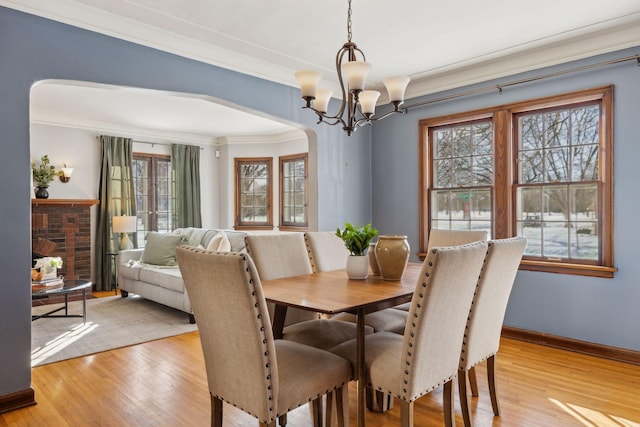 dining area featuring light wood-style floors, baseboards, arched walkways, and crown molding