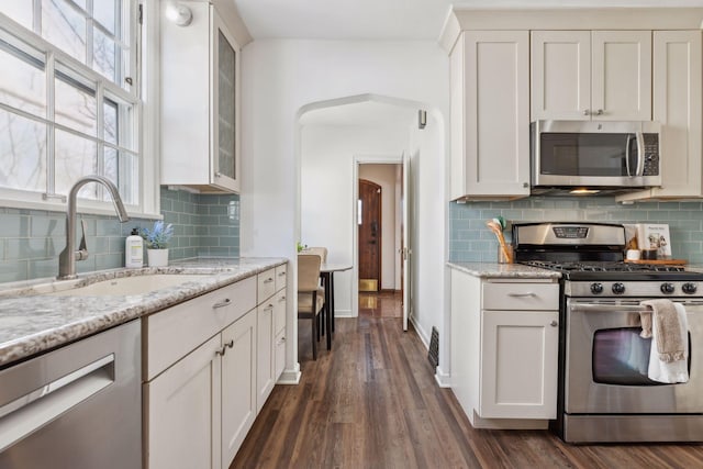 kitchen with light stone counters, appliances with stainless steel finishes, glass insert cabinets, white cabinets, and a sink