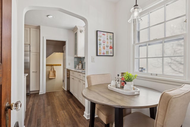 dining room featuring arched walkways, plenty of natural light, and dark wood finished floors