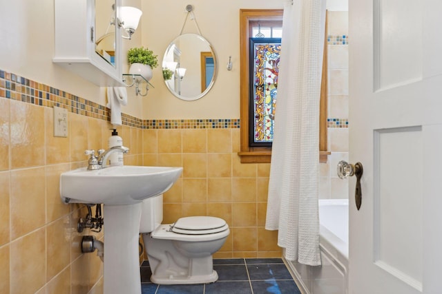 bathroom with toilet, a wainscoted wall, tile patterned floors, tile walls, and shower / tub combo with curtain