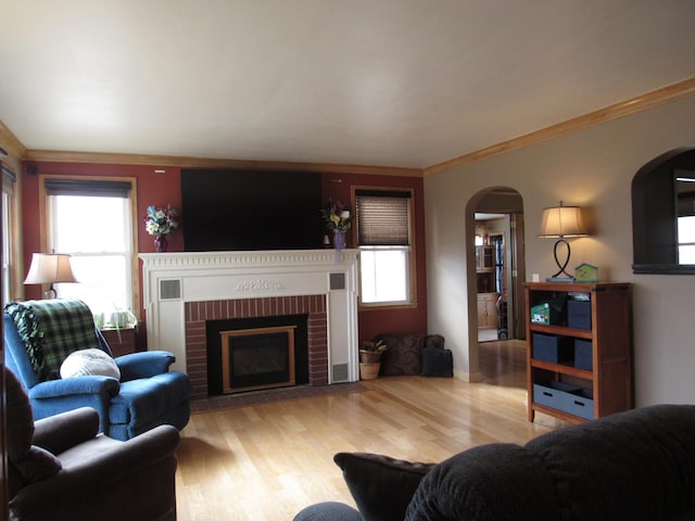 living room featuring ornamental molding, a brick fireplace, wood finished floors, and a healthy amount of sunlight