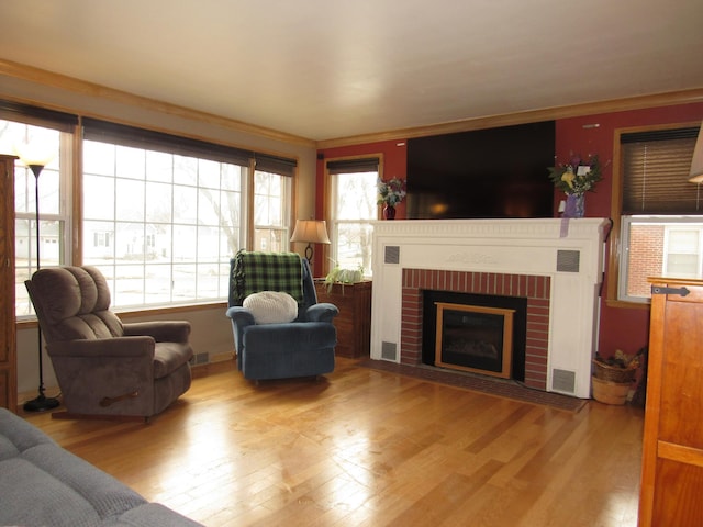 living room with light wood-type flooring, a fireplace, visible vents, and crown molding