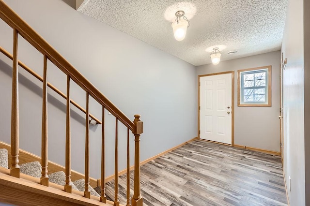 foyer featuring a textured ceiling, stairway, wood finished floors, and baseboards