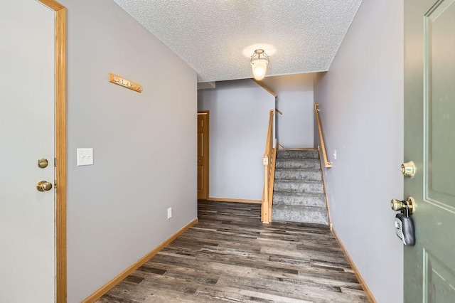 staircase featuring a textured ceiling, wood finished floors, and baseboards