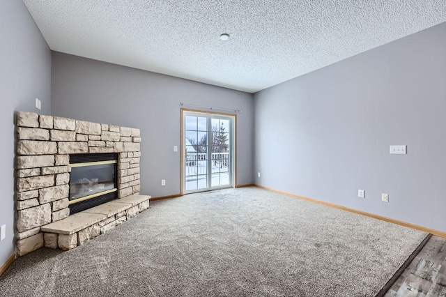 unfurnished living room with a textured ceiling, carpet floors, a stone fireplace, and baseboards