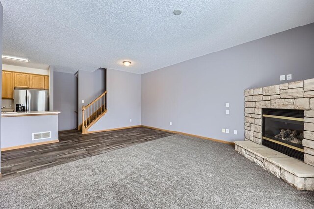 unfurnished living room featuring a textured ceiling, a stone fireplace, visible vents, and baseboards