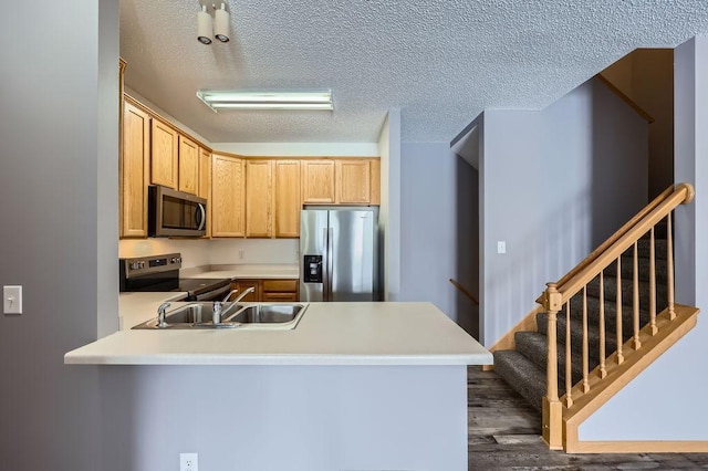 kitchen featuring stainless steel appliances, light countertops, a sink, a textured ceiling, and a peninsula