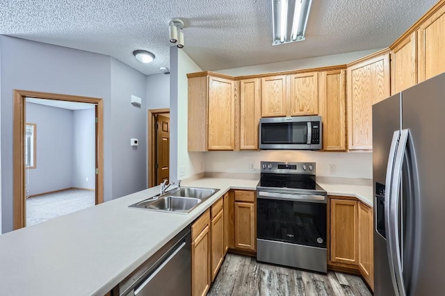 kitchen featuring stainless steel appliances, light countertops, light wood-style floors, a sink, and a textured ceiling