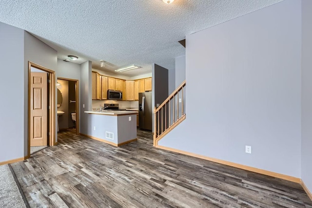 kitchen with visible vents, dark wood finished floors, a peninsula, stainless steel appliances, and light brown cabinetry