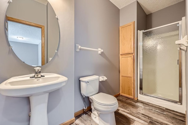 bathroom featuring a textured ceiling, toilet, wood finished floors, baseboards, and a stall shower