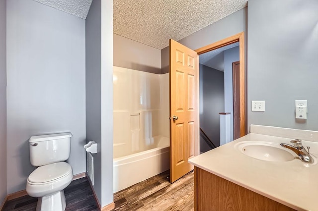 full bath with a textured ceiling, toilet, wood finished floors, vanity, and washtub / shower combination