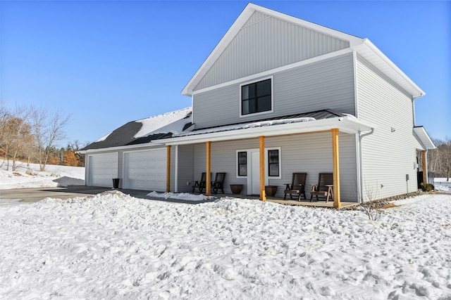 snow covered house with a porch, board and batten siding, and a garage