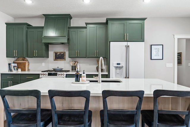 kitchen featuring light countertops, white refrigerator with ice dispenser, a kitchen island with sink, and custom exhaust hood