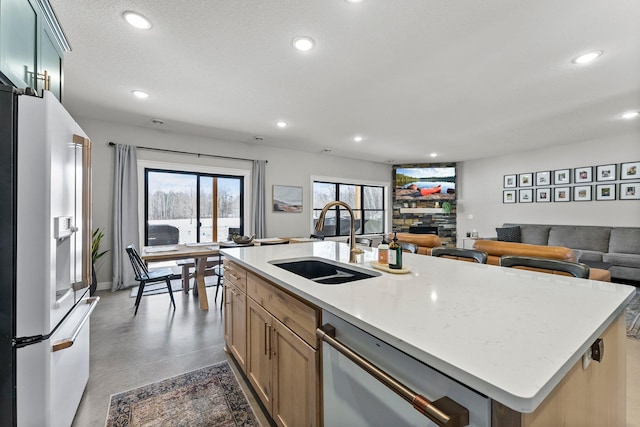 kitchen with high end refrigerator, a center island with sink, open floor plan, a sink, and stainless steel dishwasher