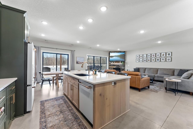 kitchen with open floor plan, a sink, a kitchen island with sink, light countertops, and stainless steel dishwasher