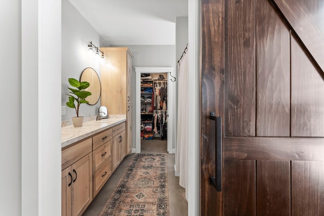 bathroom with a walk in closet, double vanity, a sink, and concrete floors