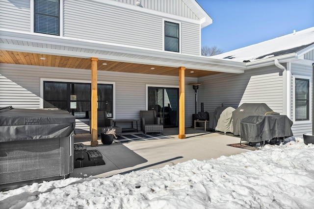 snow covered back of property featuring board and batten siding and a patio