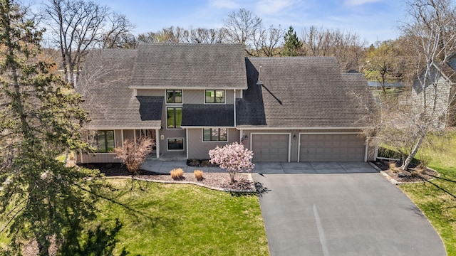 view of front of house featuring roof with shingles, a front yard, driveway, and a garage