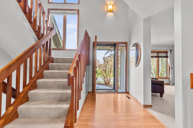 foyer with a towering ceiling, visible vents, wood finished floors, baseboards, and stairs
