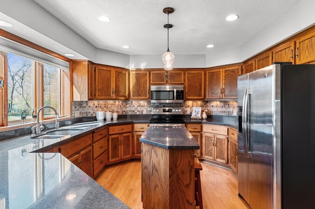 kitchen featuring appliances with stainless steel finishes, a sink, a textured ceiling, light wood-type flooring, and a kitchen island