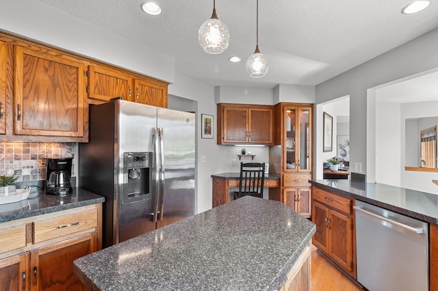 kitchen with pendant lighting, decorative backsplash, brown cabinetry, and stainless steel appliances