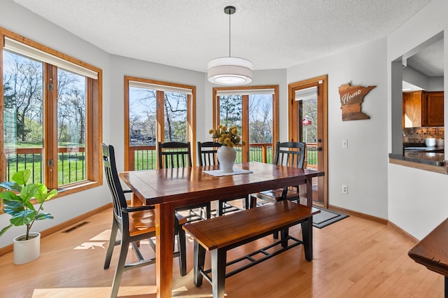 dining room with a textured ceiling, baseboards, light wood-style flooring, and visible vents