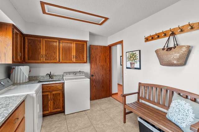 laundry room featuring a textured ceiling, cabinet space, a sink, light tile patterned floors, and separate washer and dryer