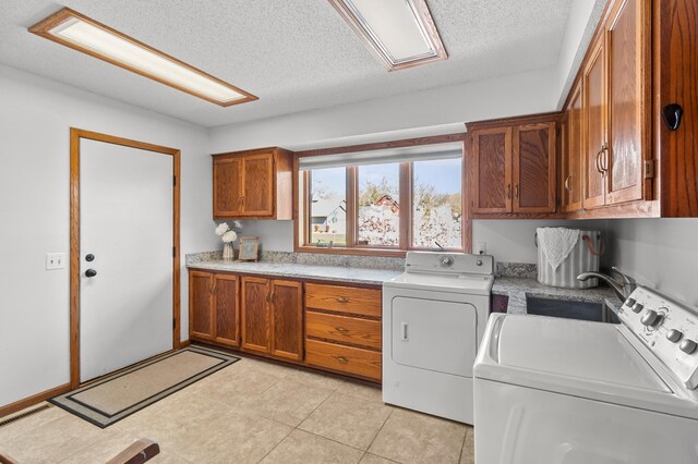 washroom with a textured ceiling, independent washer and dryer, cabinet space, a sink, and light tile patterned floors