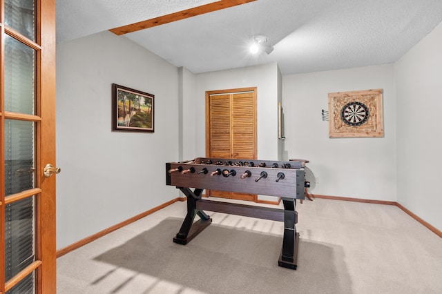recreation room with baseboards, a textured ceiling, and carpet