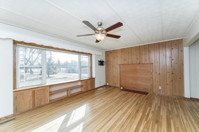 spare room with light wood-type flooring, visible vents, ceiling fan, and wooden walls