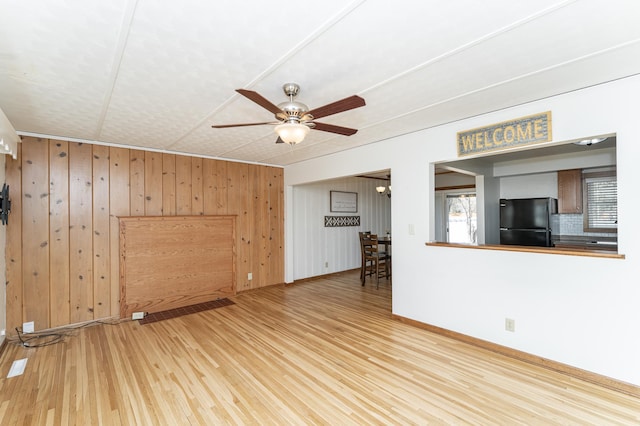 unfurnished living room with ceiling fan, wood walls, baseboards, and wood finished floors