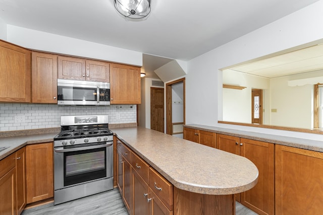 kitchen featuring stainless steel appliances, brown cabinetry, and a peninsula