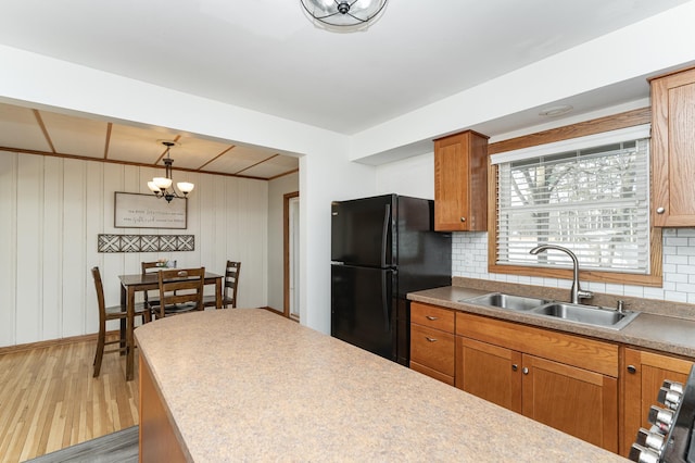 kitchen with brown cabinets, tasteful backsplash, freestanding refrigerator, a sink, and light wood-type flooring