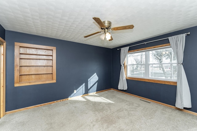 carpeted spare room with a textured ceiling, ceiling fan, built in shelves, visible vents, and baseboards