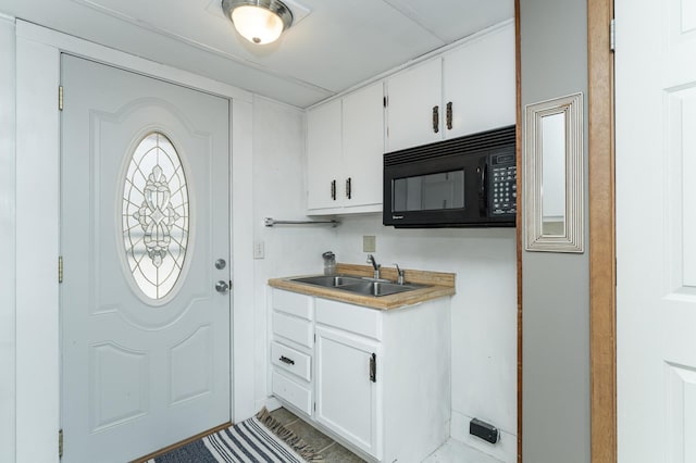 interior space with white cabinetry, black microwave, light countertops, and a sink