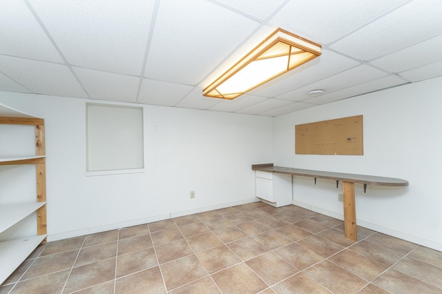 basement featuring baseboards, a drop ceiling, and tile patterned floors