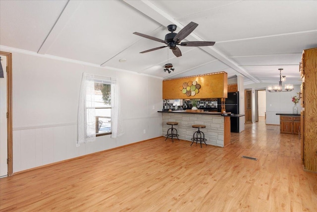 unfurnished living room featuring lofted ceiling with beams, light wood-style flooring, a wainscoted wall, ceiling fan with notable chandelier, and visible vents