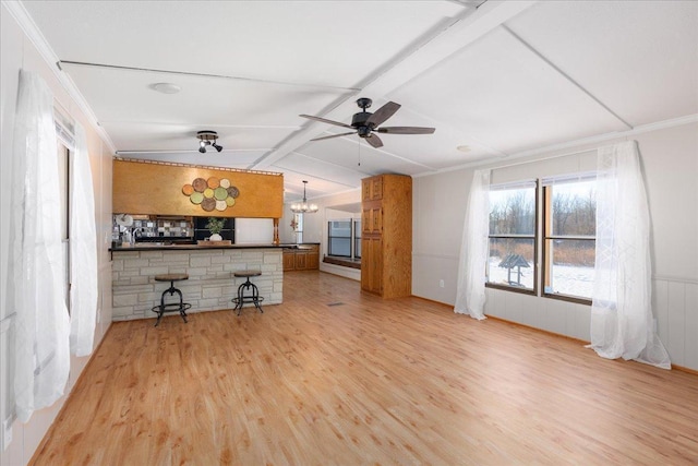 unfurnished living room featuring lofted ceiling with beams, ornamental molding, ceiling fan with notable chandelier, and light wood-type flooring