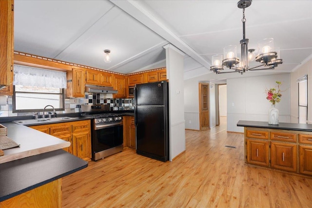 kitchen with under cabinet range hood, freestanding refrigerator, brown cabinets, stainless steel gas stove, and dark countertops