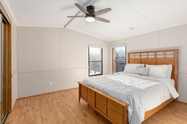 bedroom with vaulted ceiling with beams, a wainscoted wall, light wood-style flooring, and ceiling fan