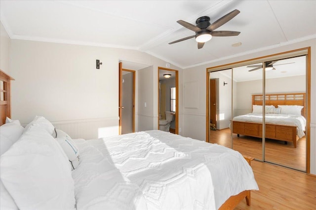 bedroom with lofted ceiling, a wainscoted wall, ornamental molding, a closet, and light wood finished floors