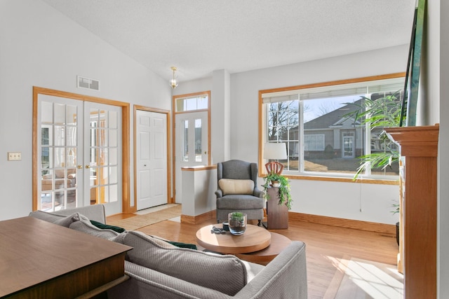 living room with french doors, lofted ceiling, visible vents, light wood-style floors, and a textured ceiling