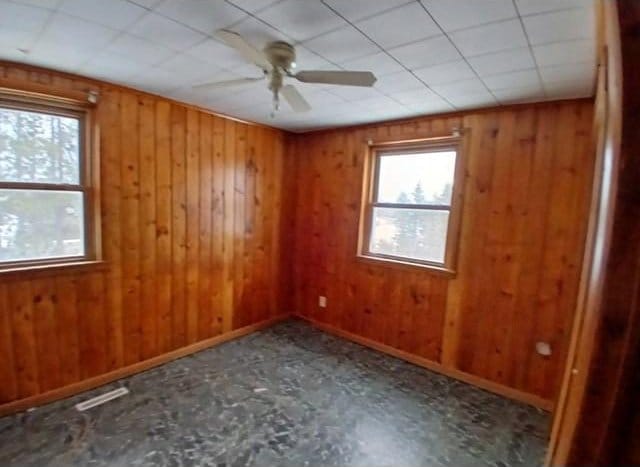 spare room with wood walls, ceiling fan, and baseboards