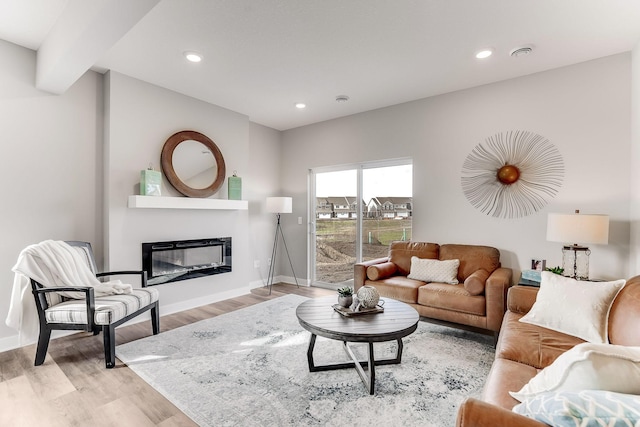 living area with light wood-style flooring, baseboards, a glass covered fireplace, and recessed lighting
