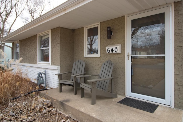 view of exterior entry with brick siding, a patio area, and stucco siding