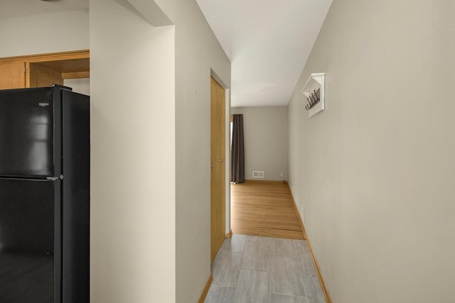 hall featuring visible vents, light wood-style flooring, and baseboards