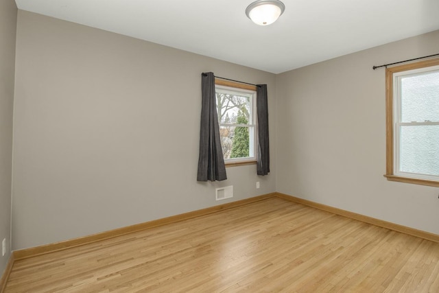 empty room featuring light wood-type flooring, baseboards, and a wealth of natural light