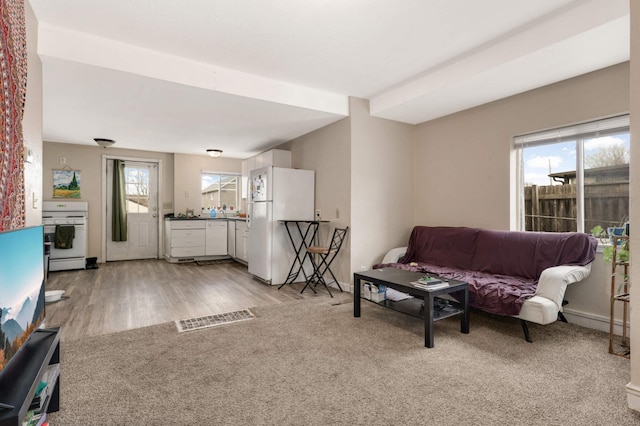 living area with light wood-type flooring, visible vents, light carpet, and baseboards