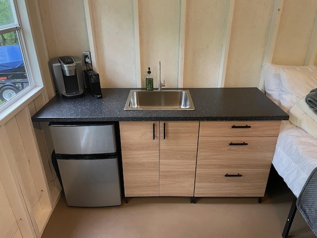 kitchen featuring dark countertops, freestanding refrigerator, light brown cabinets, and a sink