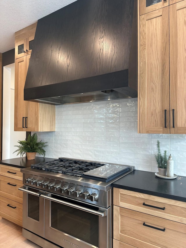 kitchen featuring range with two ovens, dark countertops, custom exhaust hood, and glass insert cabinets